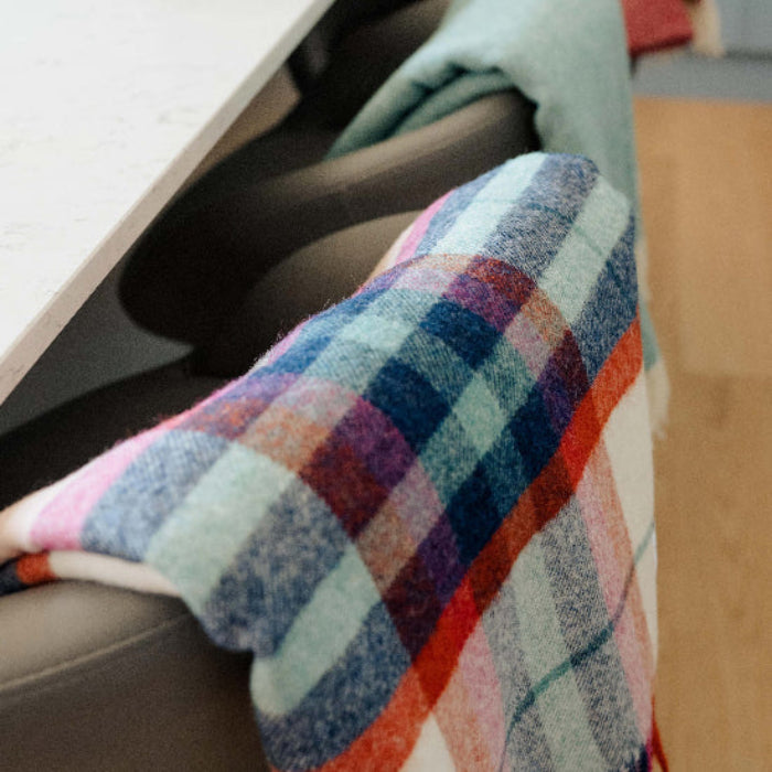 Falmouth Red & Ivory Check Shetland Wool Blanket a colorful plaid throw draped over a chair with other co-ordinating blankets in the background