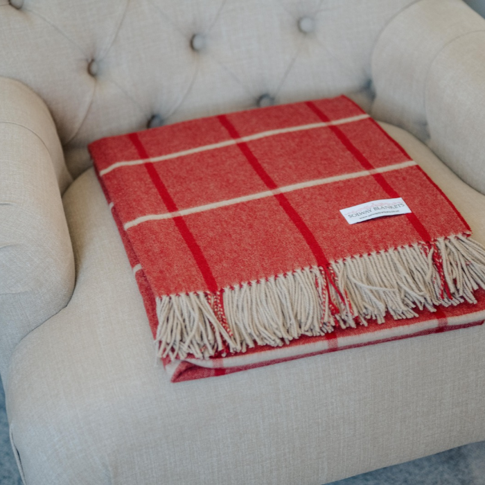 Vibrant red cashmere blanket with windowpane overcheck in red and french grey is folded neatly on a french grey linen upholstered chair