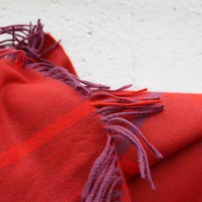 Close-up of a luxury throw, showing the red and purple herringbone weave with windowpane check in pure luxury Scottish cashmere, finished with a beautiful twisted fringe