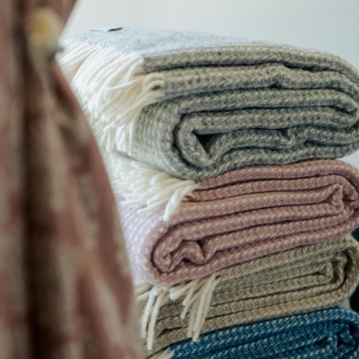 Stack of folded waffle textured wool throws featuring the extra large cloud grey throw on top – showcasing soft, sustainable style in subtle tones.