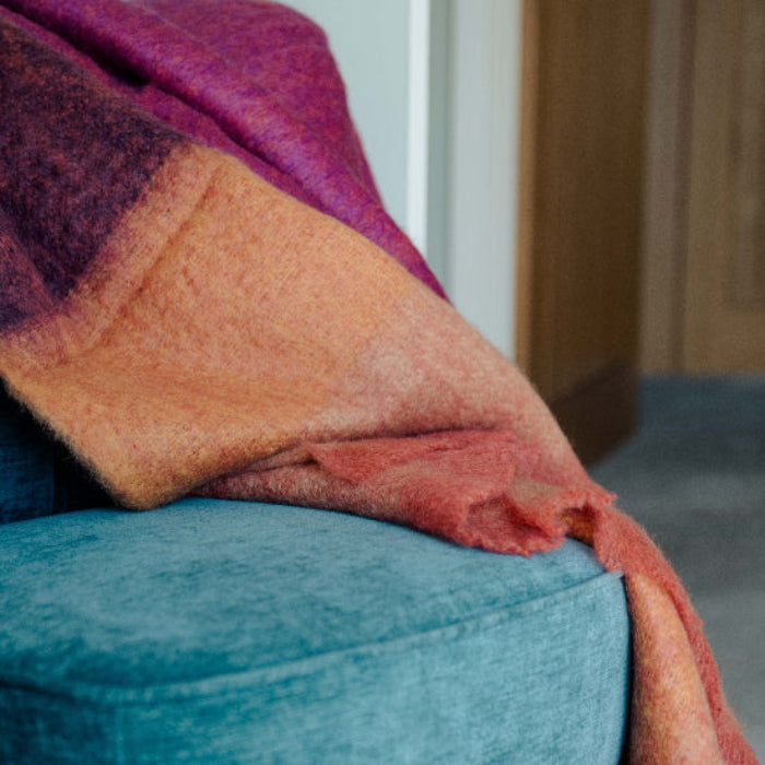 Multicolored Fuchsia Mohair Throw blanket draped over a blue chair with a neutral background