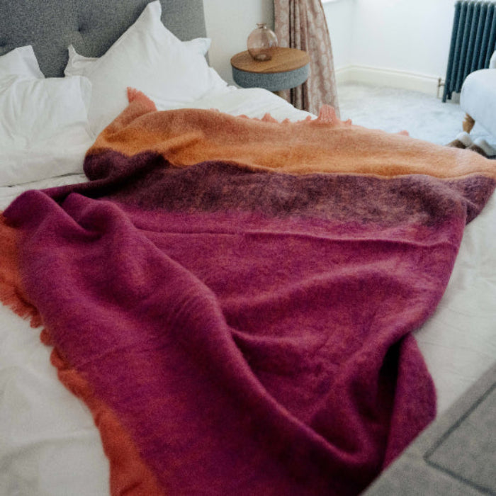 Bed with white linen and the Fuchsia Mohair Throw in colourful deep pink, burgundy and orange tones draped over it in a bedroom setting.