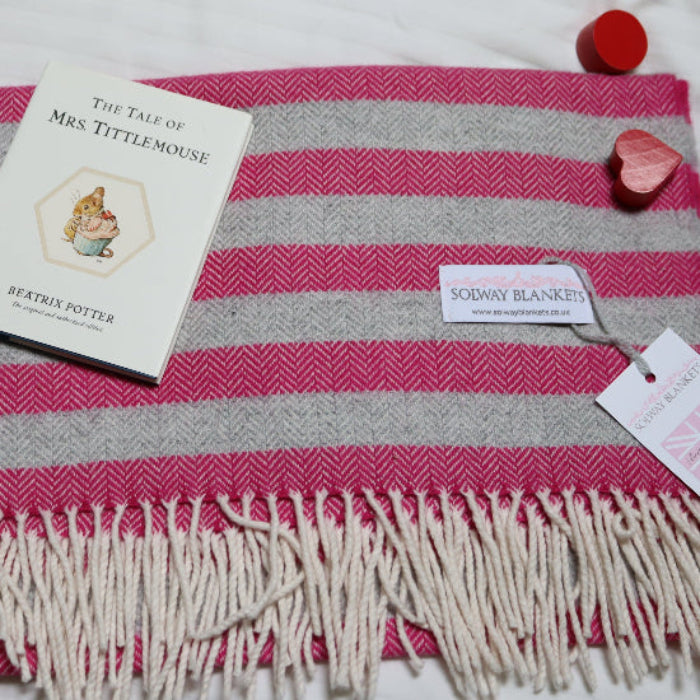 Georgina Stripe Cashmere Mix Baby Blanket a pink and gray striped blanket with a book and Solway Blankets tag on a white surface
