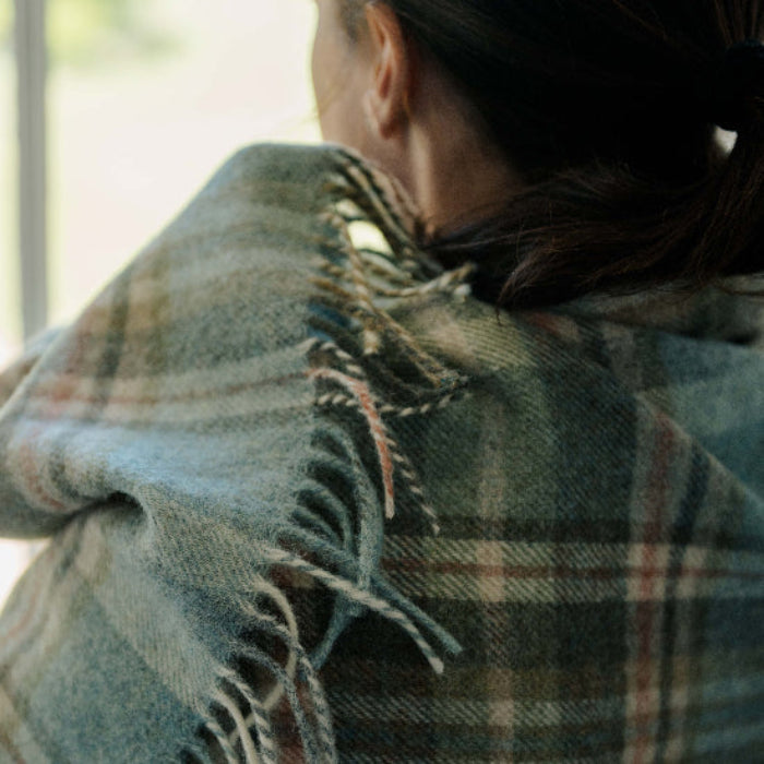 Person wearing a Glen Coe Shetland Pure New Wool Blanket draped over their shoulders looking out of a window