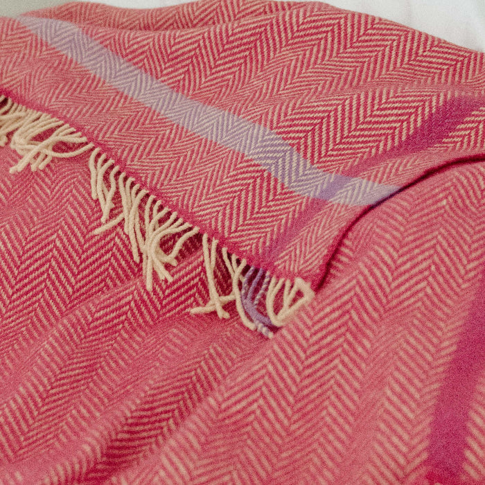 Close up of a raspberry pink and beige/cream herringbone style throw on a white bed