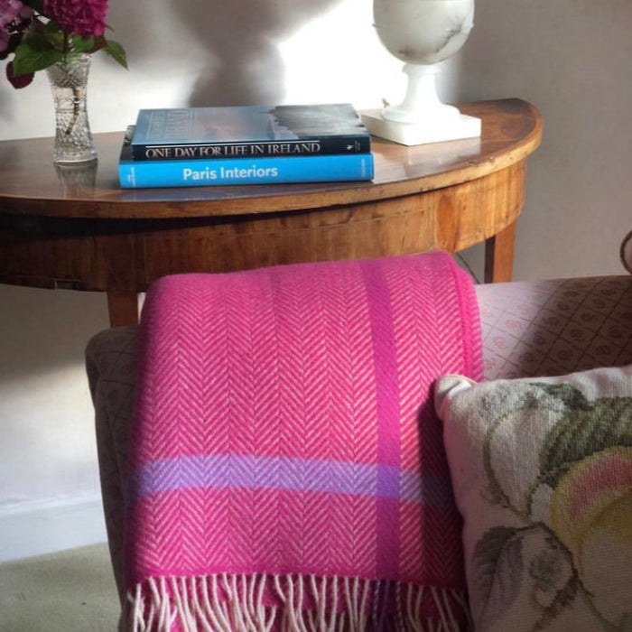 Raspberry pink plaid throw draped over a chair with books and a vase on a wooden table in the background.