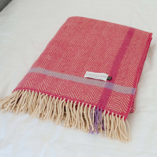 Folded raspberry pink plaid throw with fringes on a white bed