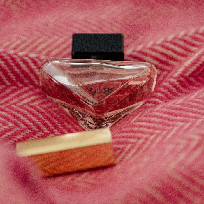 Perfume bottle on a raspberry pink and beige/cream herringbone throw