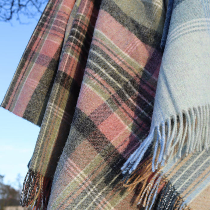 Green Kintyre Check Shetland Wool Throw with fringes and a visible brand label against a blurred natural background