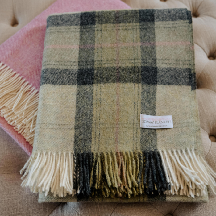 Green Skye Check Shetland Wool Throw with fringes on a couch, featuring a visible Solway Blankets brand label. Matched with a pink blanket