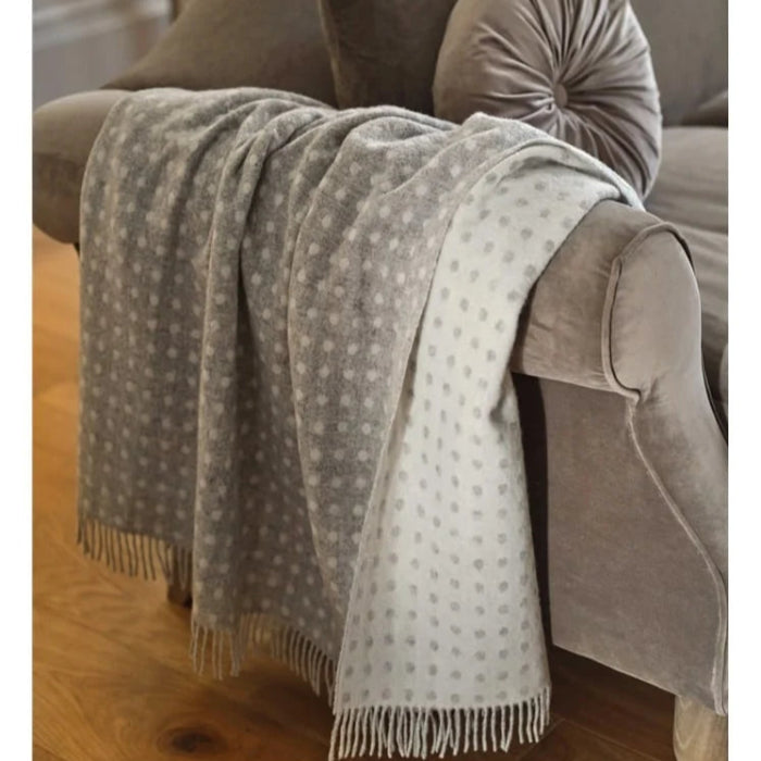 Grey and white spotted throw blanket draped over a grey chair on a wooden floor.