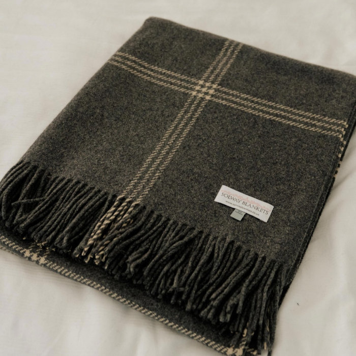 Luxury grey Scottish cashmere blanket with fine off-white overcheck and fringed edge, folded flat on white bedding with visible Solway Blankets woven label