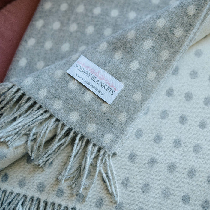 Close up folded grey and white spot throw with a Solway Blankets label on a soft chair