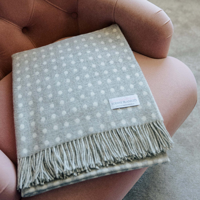 Grey and white spot throw with fringes folded neatly on a soft chair