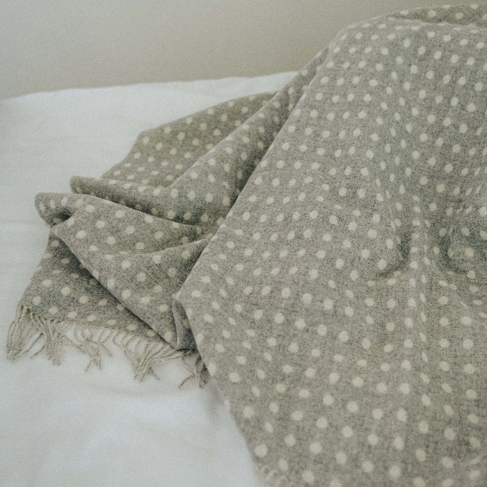 grey and white spot lambswool throw with fringes on a white bed