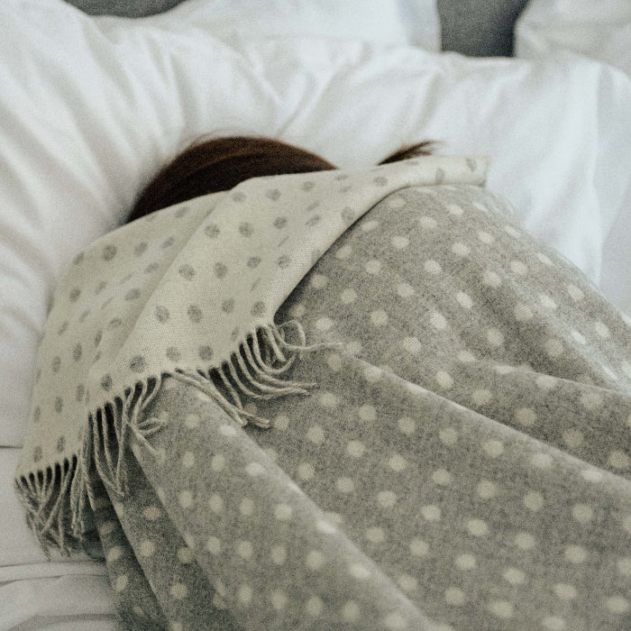 Person wrapped in a grey and white reversible throw on a bed