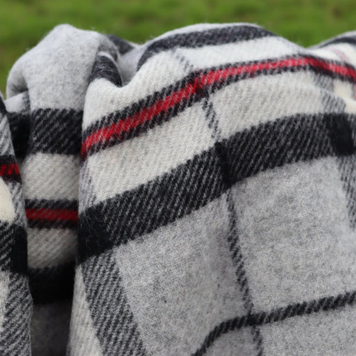 Grey Thompson Tartan Pure New Wool Blanket with grey, black and red colours forming a check plaid design on a blurred green background