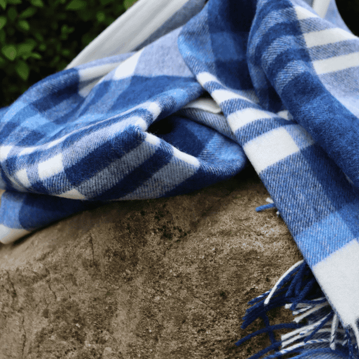 Blue and white checkered blanket throw draped over a stone surface with greenery in the background