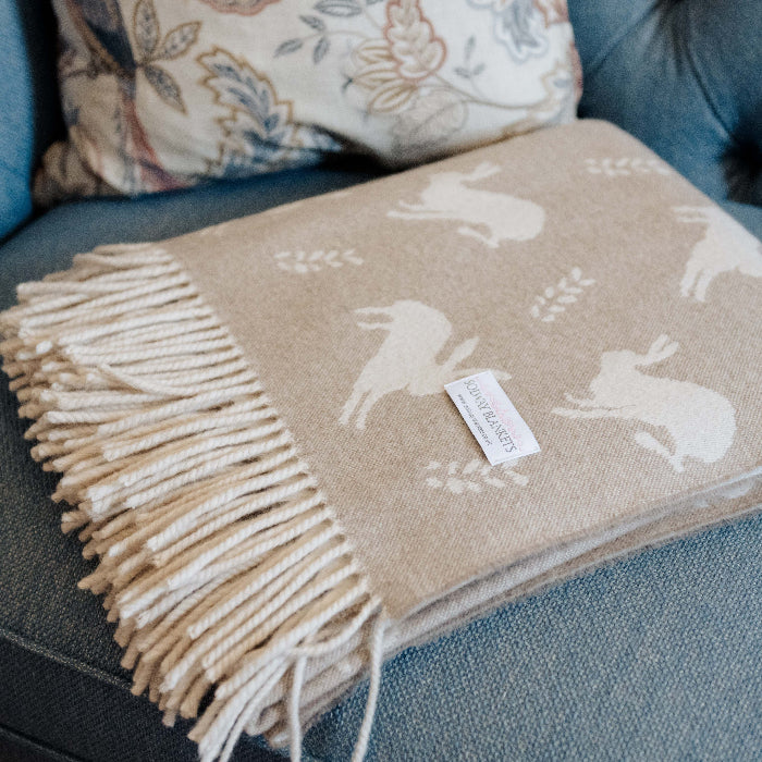 Beige lambswool throw with hare pattern and fringe folded neatly with Solway Blankets label on a blue couch