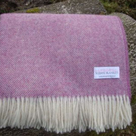 Pink Heather Herringbone Shetland Woven Wool Blanket with white fringe on a stone surface