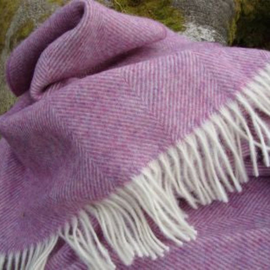 Purple Heather Herringbone Shetland Wool Blanket with white fringe draped over a surface