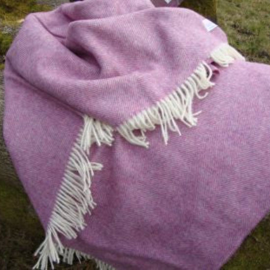 Heather Herringbone Shetland Wool Woven British Blanket with white fringe draped over a tree branch on a grassy background