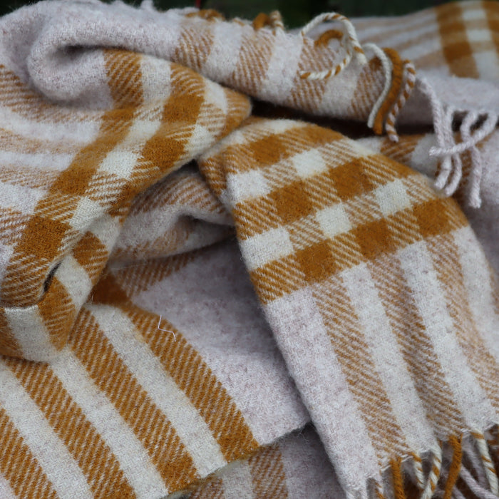 Close up of a mustard and oatmeal check wool blanket placed on a stone wall
