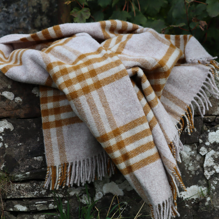 Mustard and oatmeal check wool blanket with fringe draped over a stone wall