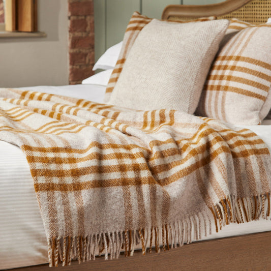 Plaid mustard and oatmeal coloured blanket draped over a bed with pillows in a cosy bedroom setting.