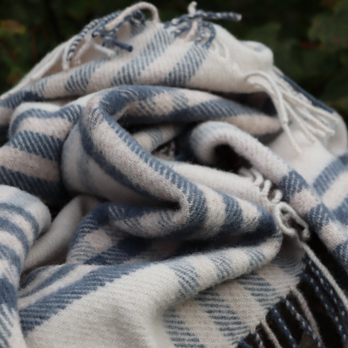 Blue plaid wool blanket with fringe bundled on a blurred natural background