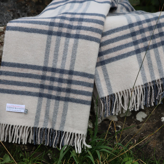 Plaid blue wool blanket with fringes displaying a Solway Blankets label draped over a stone surface