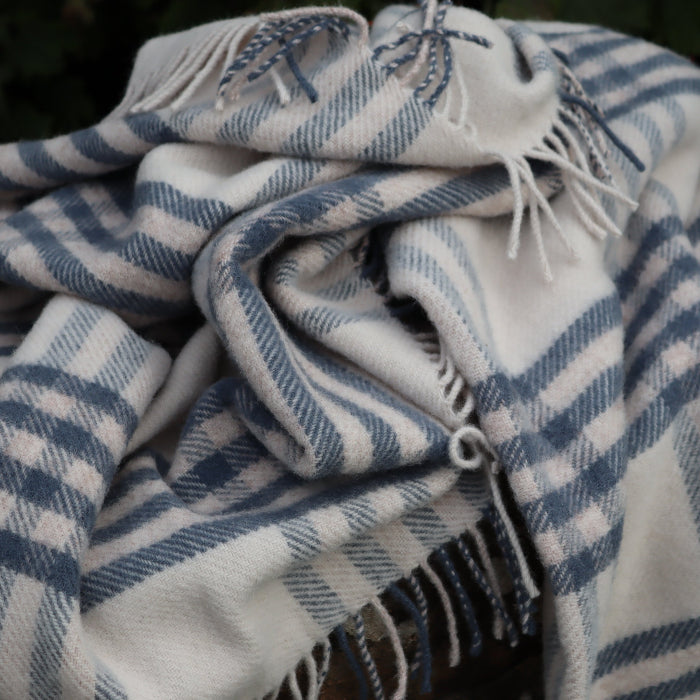 Plaid blue wool blanket with white fringe on a stone wall