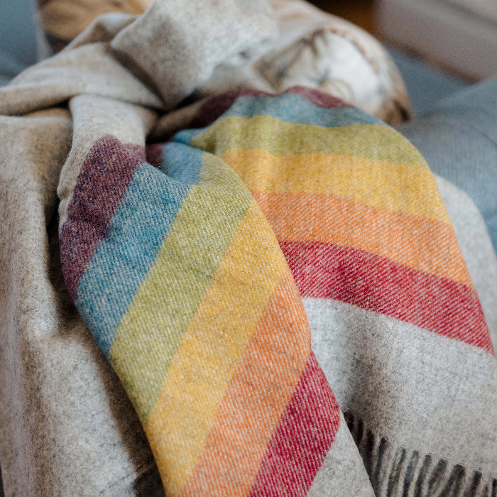 Highland Horizon Shetland Wool Rainbow Stripe Blanket colourful grey blanket with rainbow stripe draped over  a couch.