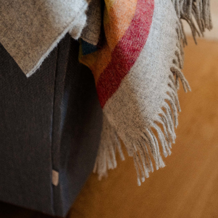 Close-up of the Highland Horizon Shetland Wool Rainbow Stripe Blanket a colourful blanket draped over an armchair, showing textured fringe 
