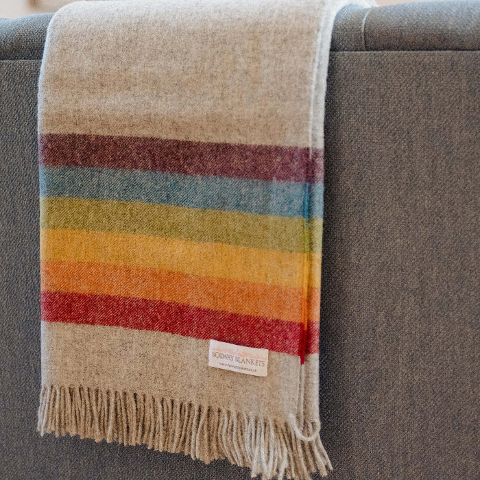 Colorful rainbow striped blanket draped over a gray sofa with a visible Solway Blankets brand label.