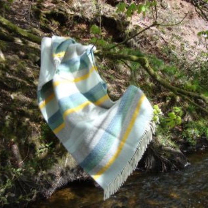 Colourful striped wool blanket draped over a tree branch by a stream