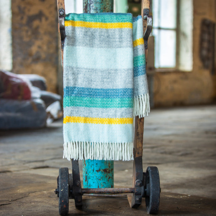 Wool blanket with colourful stripes of blue, green, yellow, white and grey on a cart in an industrial setting