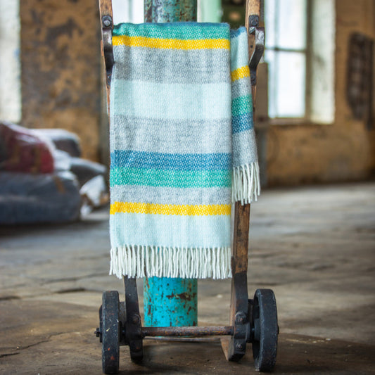 Wool blanket with colourful stripes of blue, green, yellow, white and grey on a cart in an industrial setting