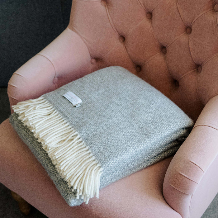 Grey wool blanket with white fringes folded neatly on a pink tufted chair.