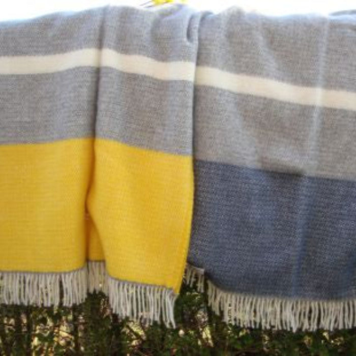 Grey and yellow plaid wool blanket with fringes draped over a hedge next to a similar wool blanket with blue and grey colours