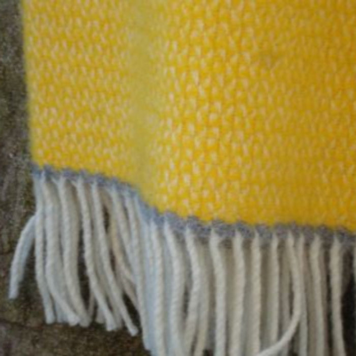 Close up of a yellow and grey wool blanket with fringed edge on a textured surface