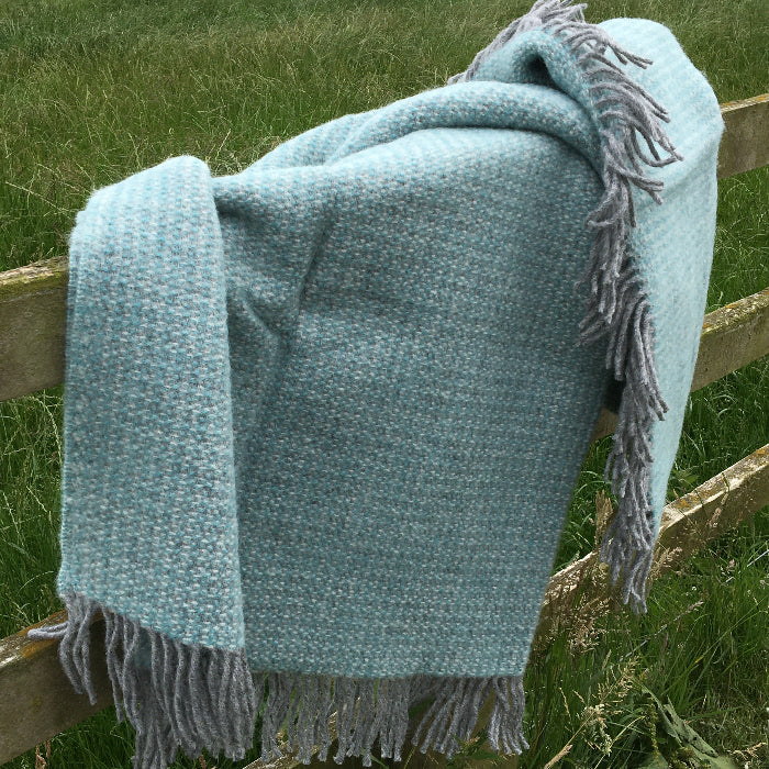 Spearmint and grey soft wool blanket throw draped over wooden fence outside in a grassy field 