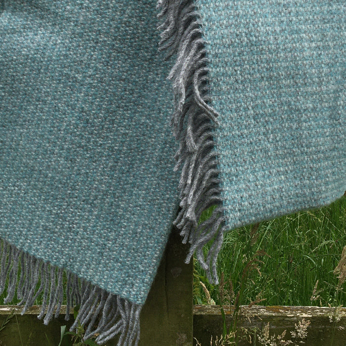 Spearmint and grey soft wool blanket throw with fringes draped over a wooden fence outdoors