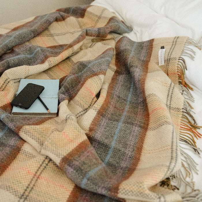 Plaid throw draped over a bed with a phone and notebook on top