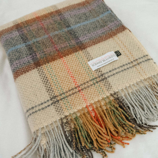 close up of a folded plaid throw with fringes on a white background displaying the Solway Blankets label