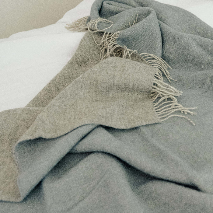 Blue and light grey reversable blanket with frayed edged fringe draped over white bedding