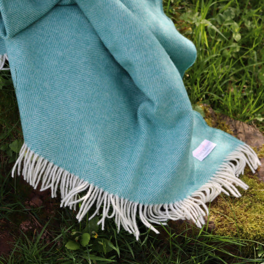 Jade Green Herringbone Shetland Wool Throw Blanket with white fringe on a grassy surface