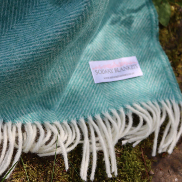 Jade Green Herringbone Shetland Wool Throw blanket with white fringe on a natural background