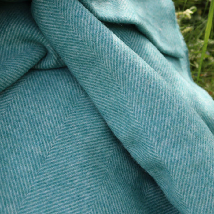 Close-up of Jade Green Herringbone Shetland Wool Throw with a herringbone pattern on grass.
