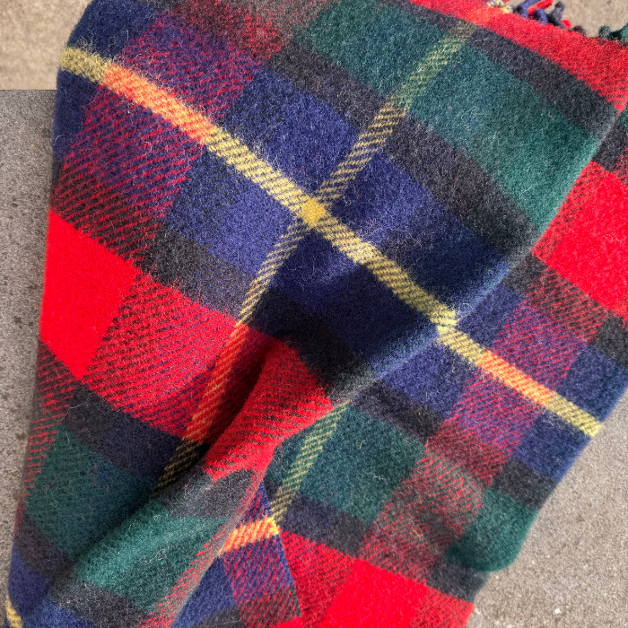 A close-up of a folded Kilgour Wool Knee blanket, featuring a tartan pattern with red, green, navy blue, black, and thin yellow stripes.